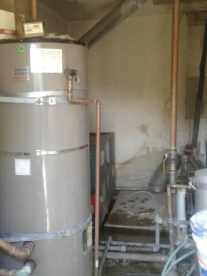 A large commercial storage tank water heater with copper supply lines and a flue in a concrete utility room