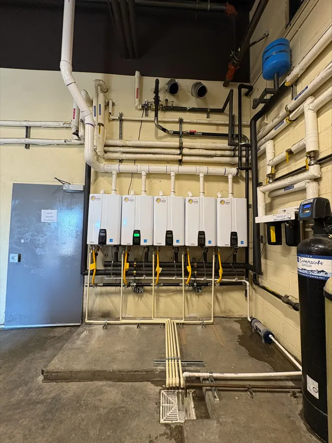 Five wall-mounted tankless water heaters beside an Eversoft water softener tank in a commercial utility room